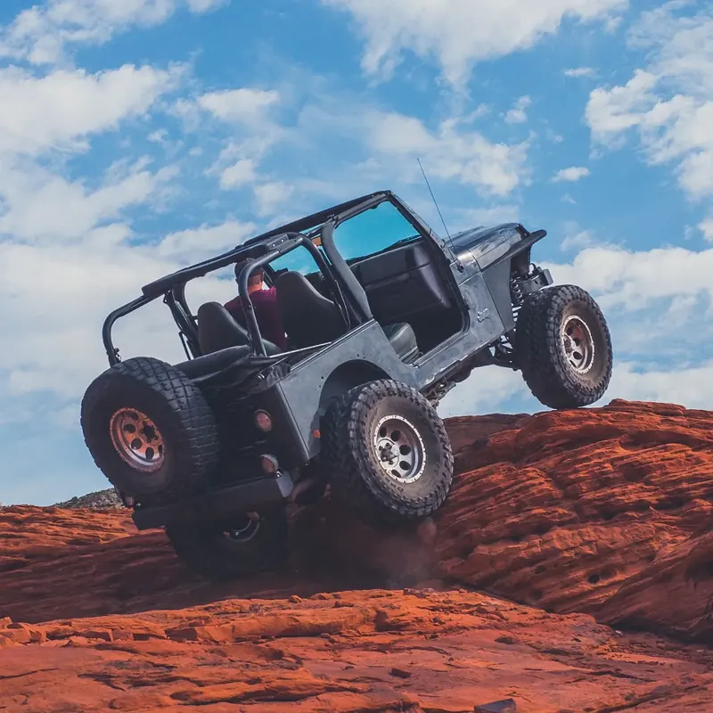 Open-top Jeep with gears and lockers climbing red sandstone
