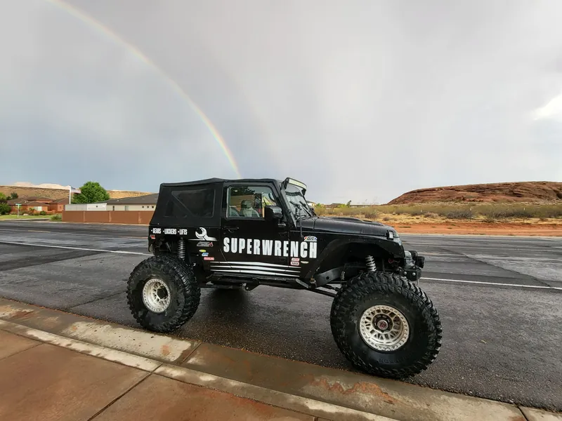 Super Wrench branded Jeep parked beneath a rainbow