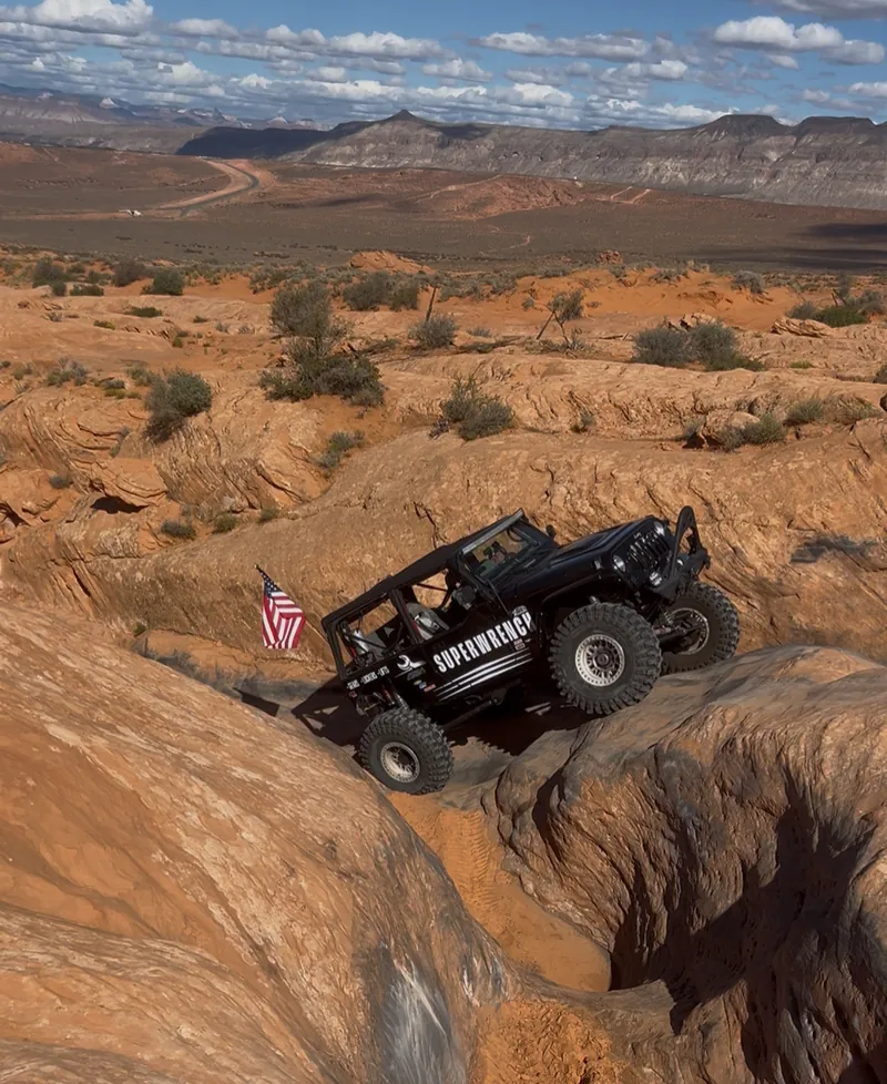 Black Jeep on sandstone with a wide desert view behind it